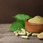 Kratom in capsules and in a wooden bowl.