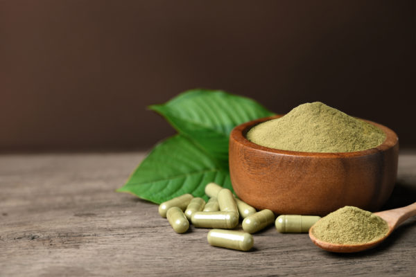 Kratom in capsules and in a wooden bowl.